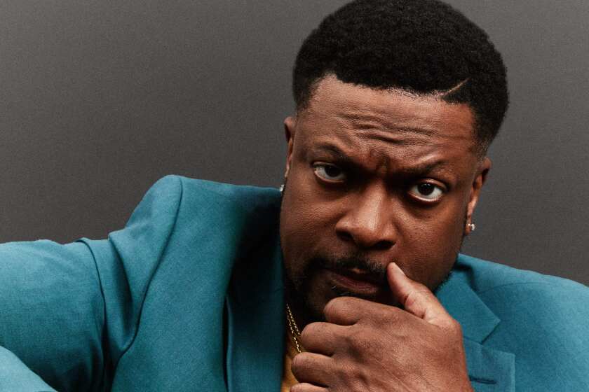 Chris Tucker poses for a portrait. He has his hand resting against his face and thumb against his nose. 