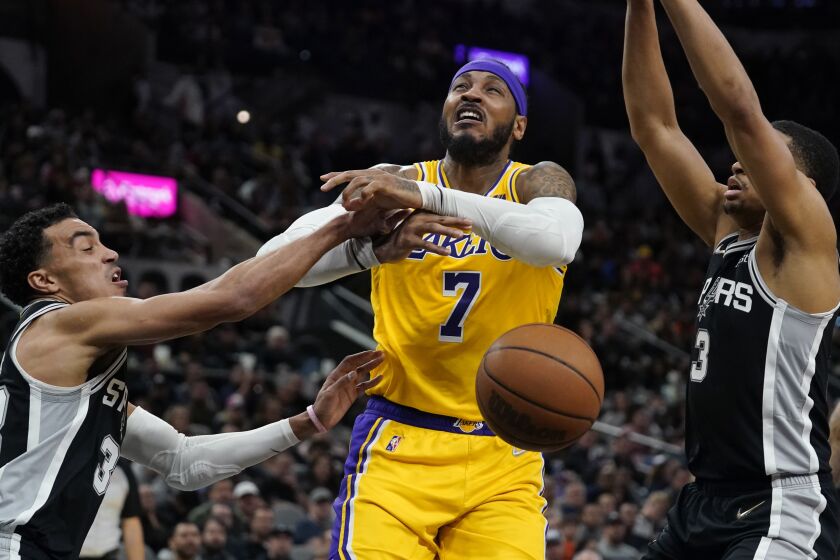 Los Angeles Lakers forward Carmelo Anthony (7) is fouled as he drives to the basket against San Antonio Spurs guard Tre Jones, left, and forward Keldon Johnson (3) during the first half of an NBA basketball game, Monday, March 7, 2022, in San Antonio. (AP Photo/Eric Gay)