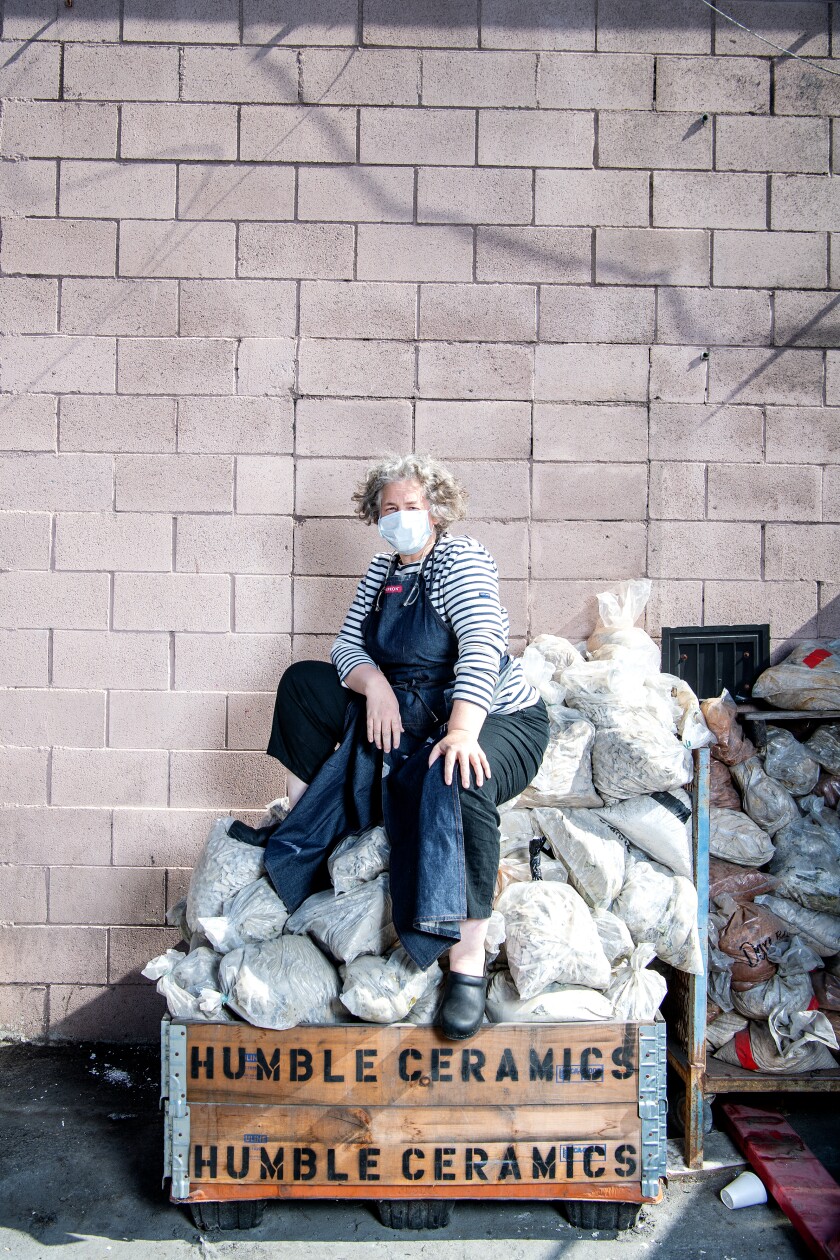 Delphine Lippens sits on a pile of white cloth bags in a cart marked "Humble Ceramics."
