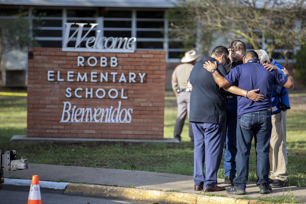 Men pray outside Robb Elementary School in Uvalde, Texas, the day after a gunman killed 19 children and two teachers.