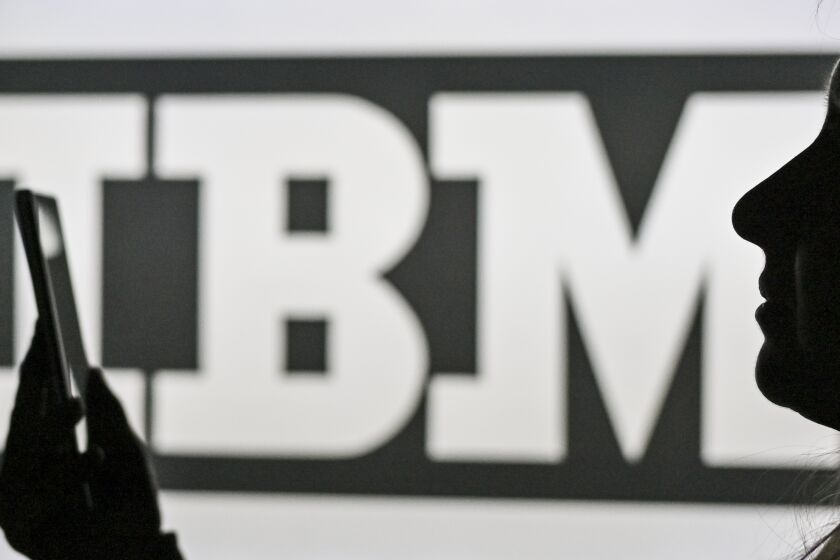 An image of a woman holding a cell phone in front of the IBM logo displayed on a computer screen. On Tuesday, January 12, 2021, in Edmonton, Alberta, Canada. (Photo by Artur Widak/NurPhoto via AP)
