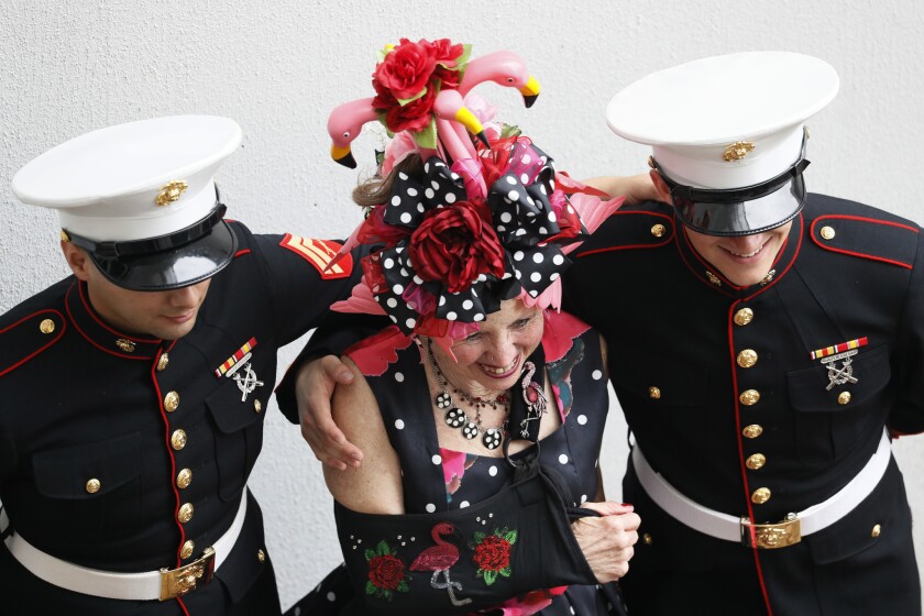 한 여성이 2019 년 5 월 4 일 처칠 다운스에서 열리는 켄터키 더비 경마 145 회 달리기 동안 두 명의 군인과 함께 포즈를 취하는 동안 장식용 모자를 착용합니다.