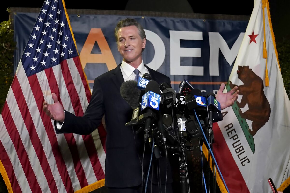 Gov. Gavin Newsom stands behind a cluster of microphones