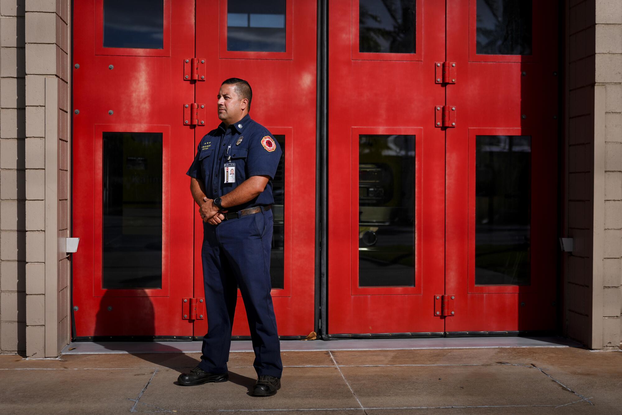 A fire captain stands in front of a set of red doors. 