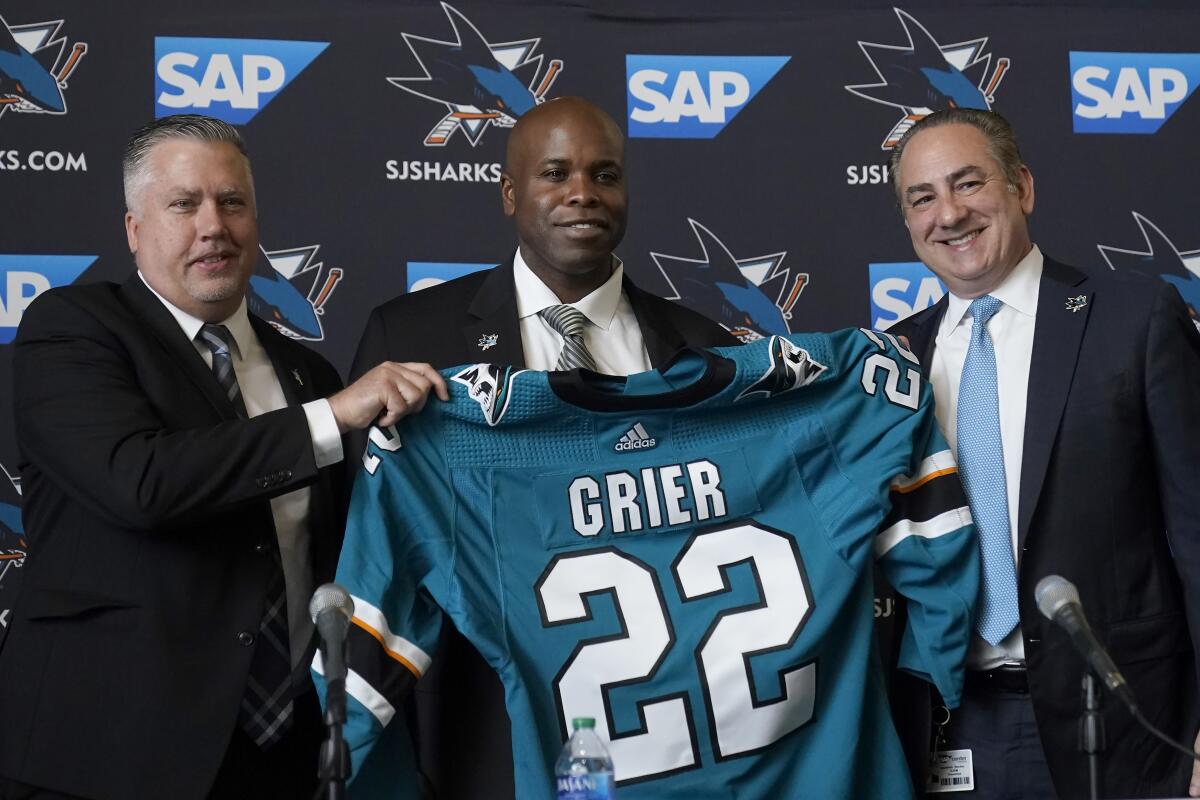 Mike Grier, middle, poses for photos as he is introduced as the new general manager of the San Jose Sharks between assistant general manager Joe Will, left, and president Jonathan Becher at a news conference in San Jose, Calif., Tuesday, July 5, 2022. (AP Photo/Jeff Chiu)
