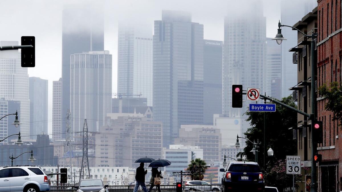 Pedestrians cross 1st Street in Boyle Heights as rain clouds partially obscure the downtown L.A. skyline during a storm on March 6.