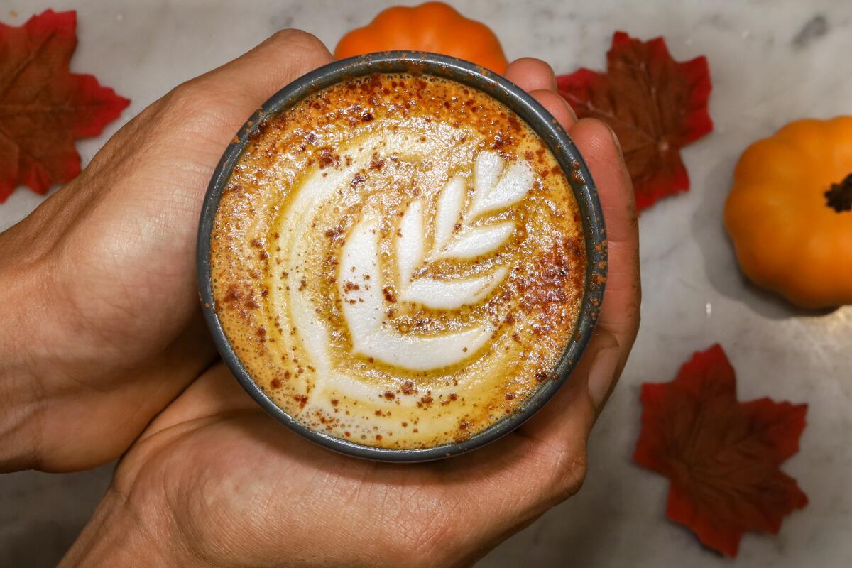 Hands cup a pumpkin spice latte topped with decorative foam