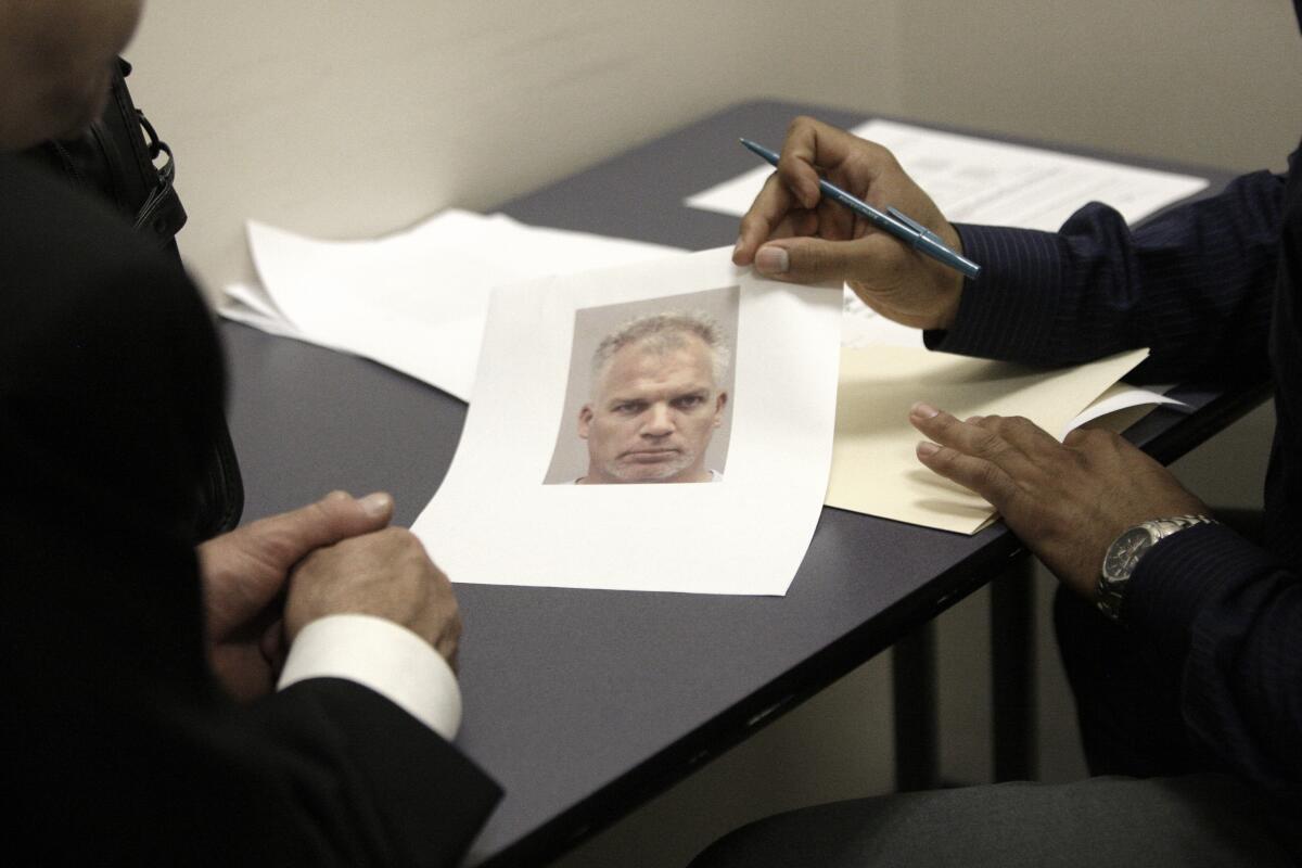 The hands of two people at a table as one shows a mugshot 