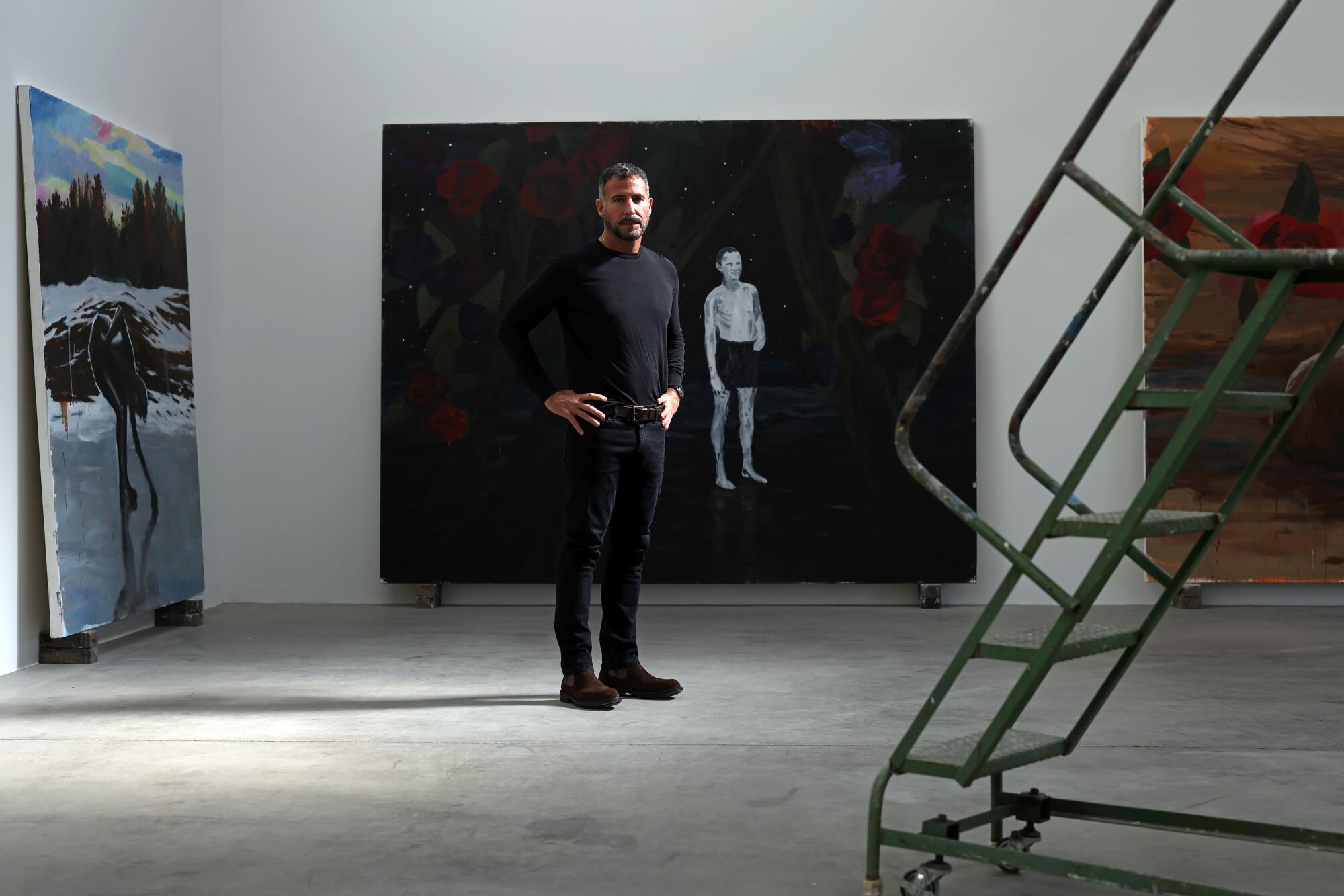 A man stands in a gallery next to a staircase on wheels 