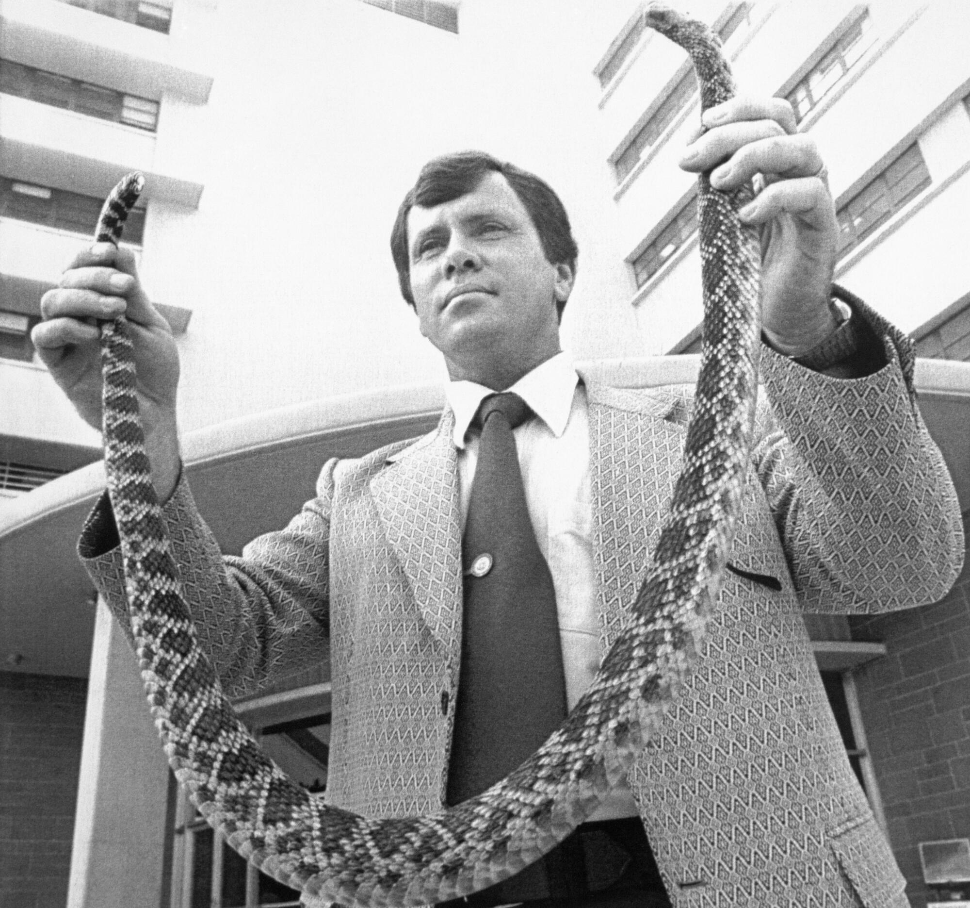 A man holds up a snake with his two hands.