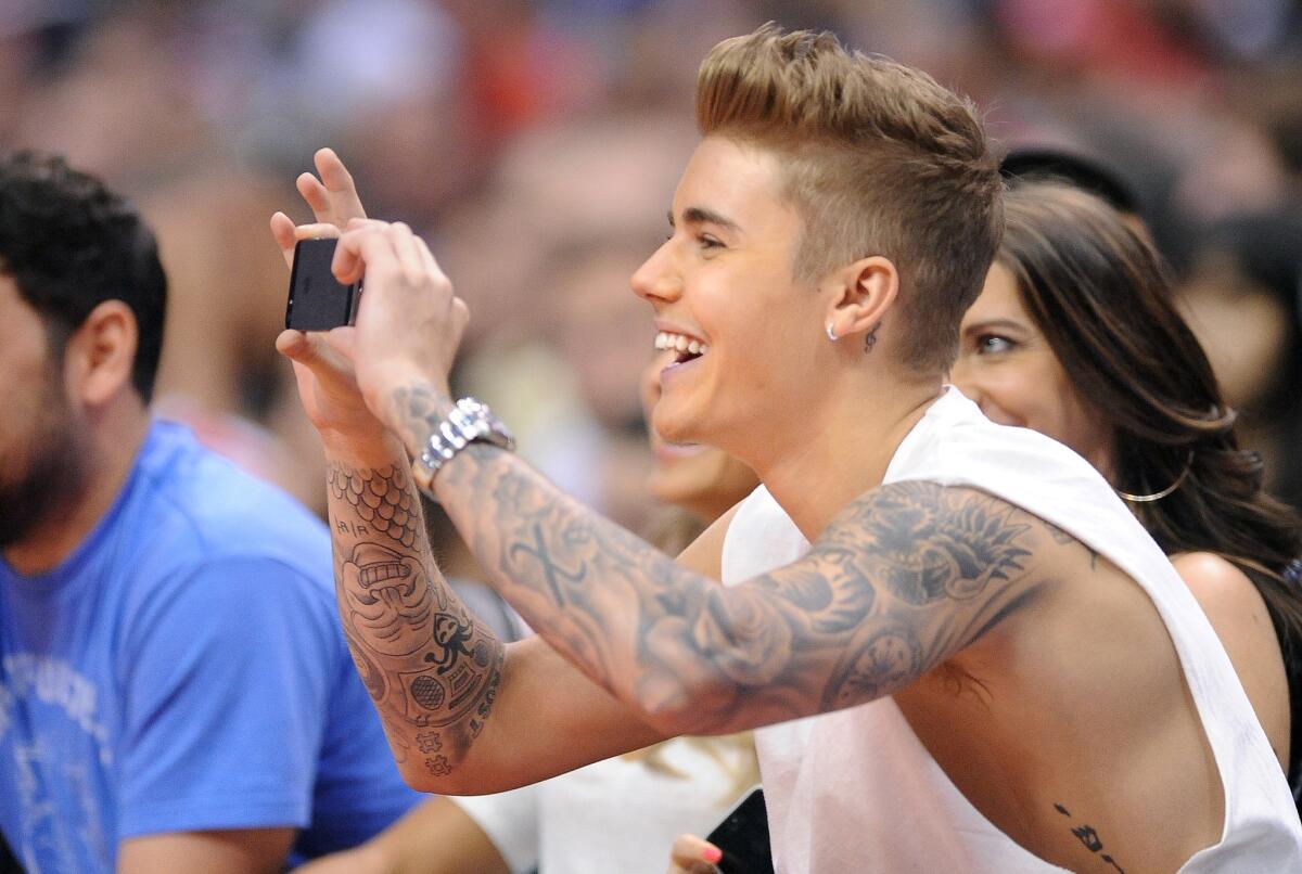 Singer Justin Bieber, who is to appear at a private Calvin Klein concert, takes a picture with his phone during a timeout at a Clippers game in this file photo.