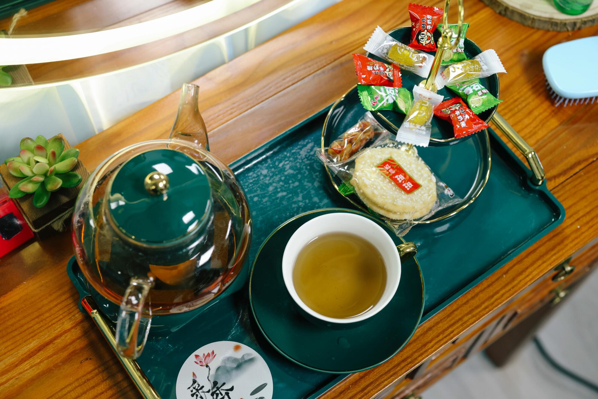 A tray of tea in a cup and a glass teapot, with assorted snacks
