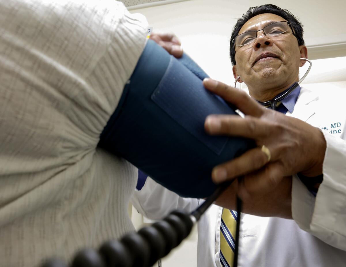 A doctor with a stethoscope checks the blood pressure of a patient.