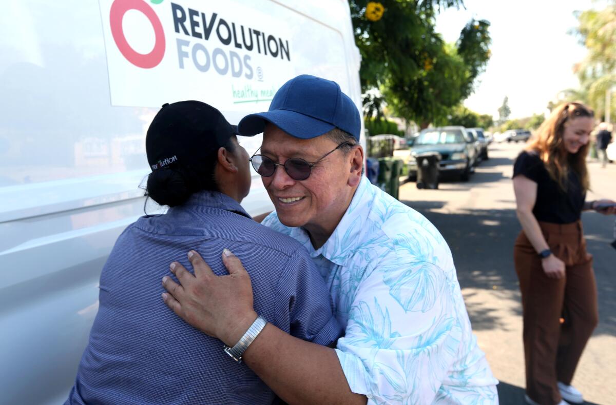 A woman, pictured from behind, hugging a man beside a white van with a logo reading "Revolution Foods"