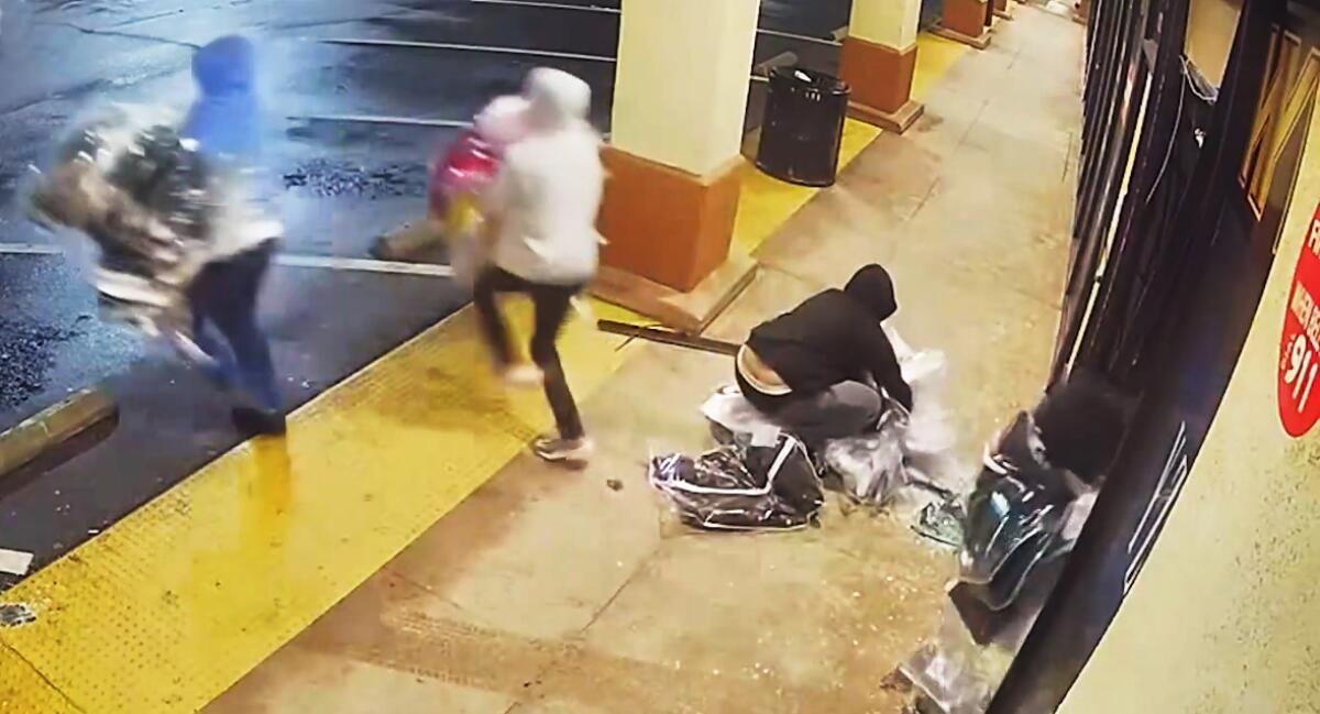 People in hoodies run away from a storefront with their arms filled with merchandise. 