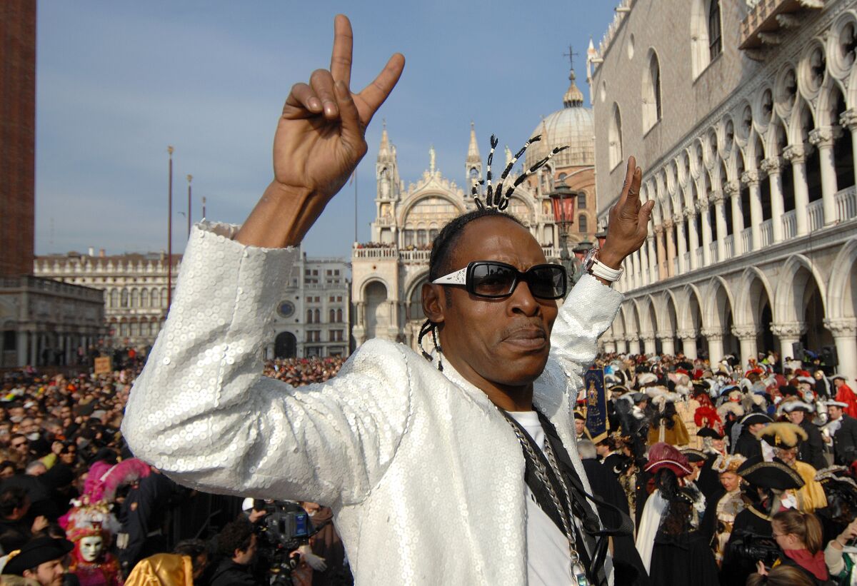 With hands up displaying peace signs, Coolio poses in a spangled white jacket with Venice's Saint Marks Square behind him. 