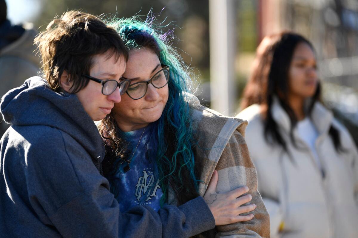 Two people comfort one another at a crime scene.