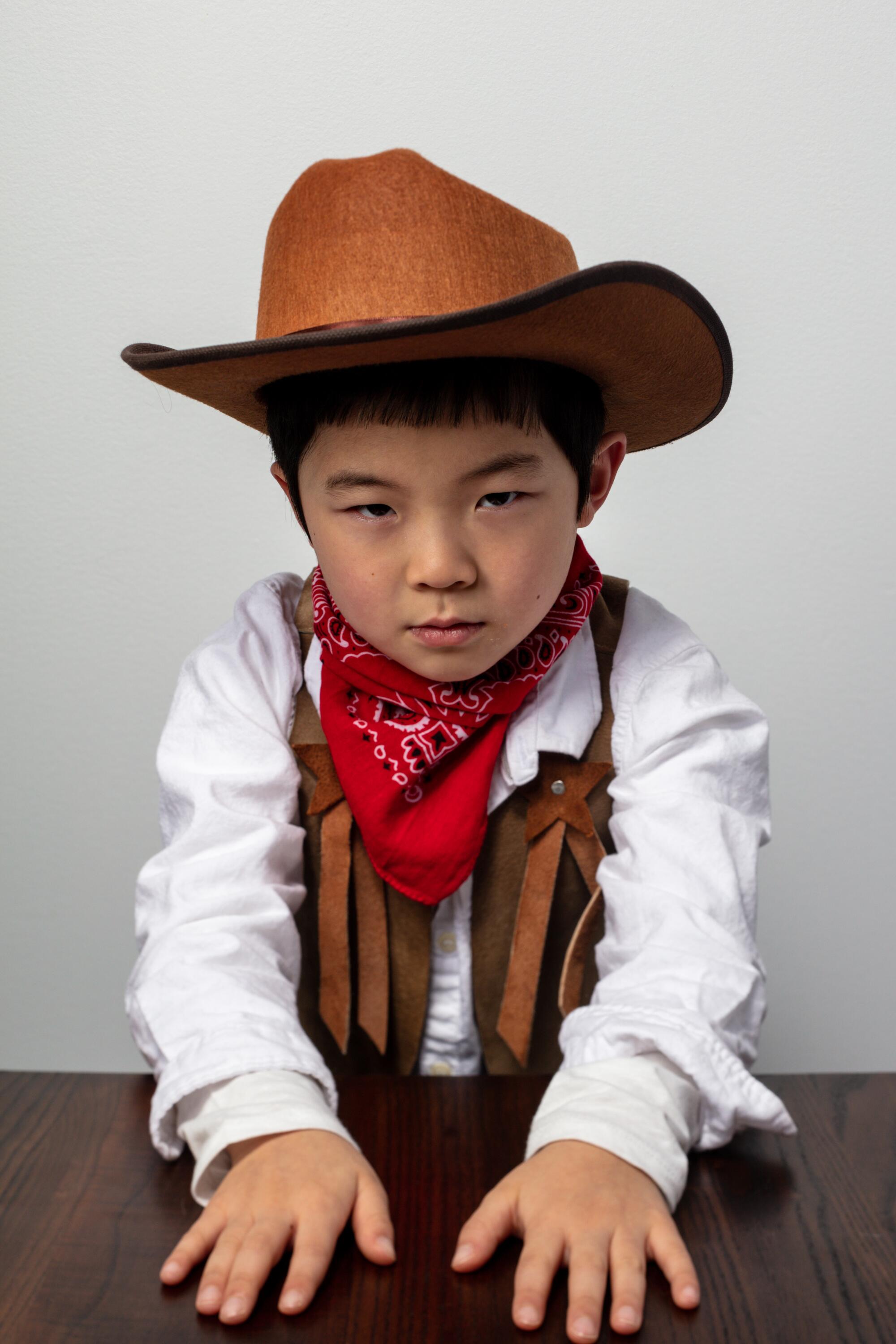 Alan Kim, in a cowboy costume, places his cards, or his hands, at least, on a table, western style.