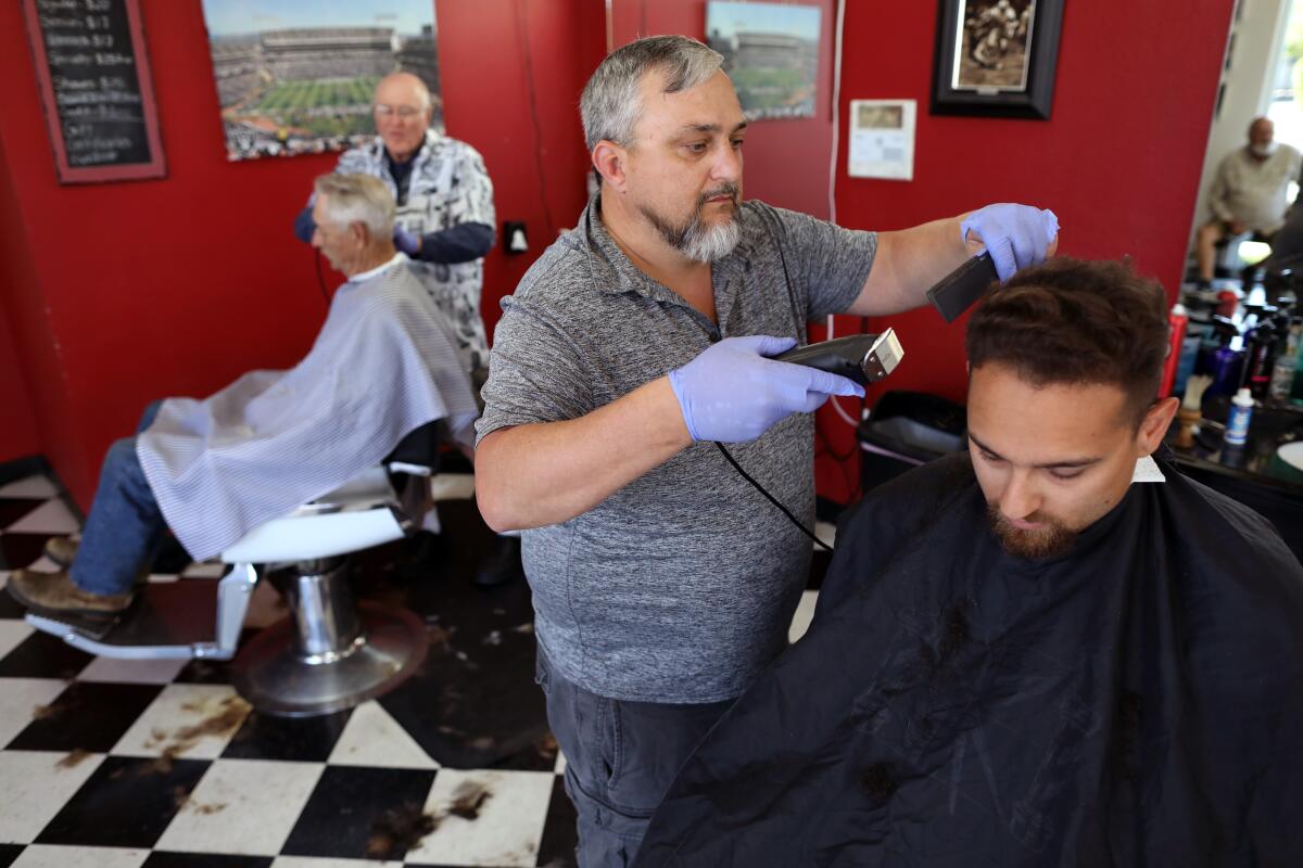 Wes Heryford, centro, propietario de Butte House Barber Shop en el condado de Sutter, atiende a Ben Martin, de 25 años. Heryford no exige que sus clientes o barberos usen máscaras, y no le preocupa infectarse con el nuevo coronavirus.