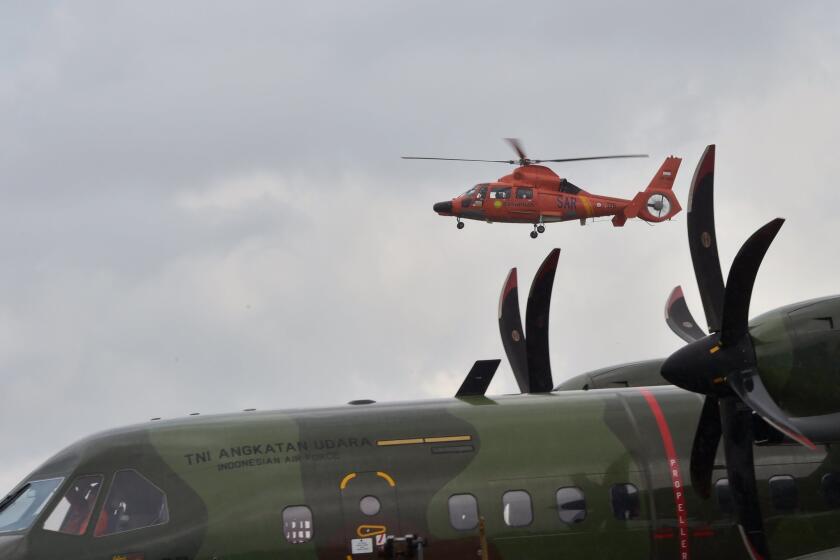 An Indonesian search and rescue helicopter flies Monday above an air force plane carrying the bodies of passengers of Indonesia AirAsia Flight 8501.