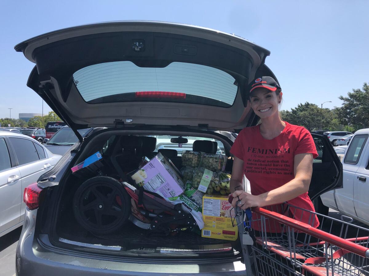 A woman standing with a shopping cart next to a car filled with groceries.