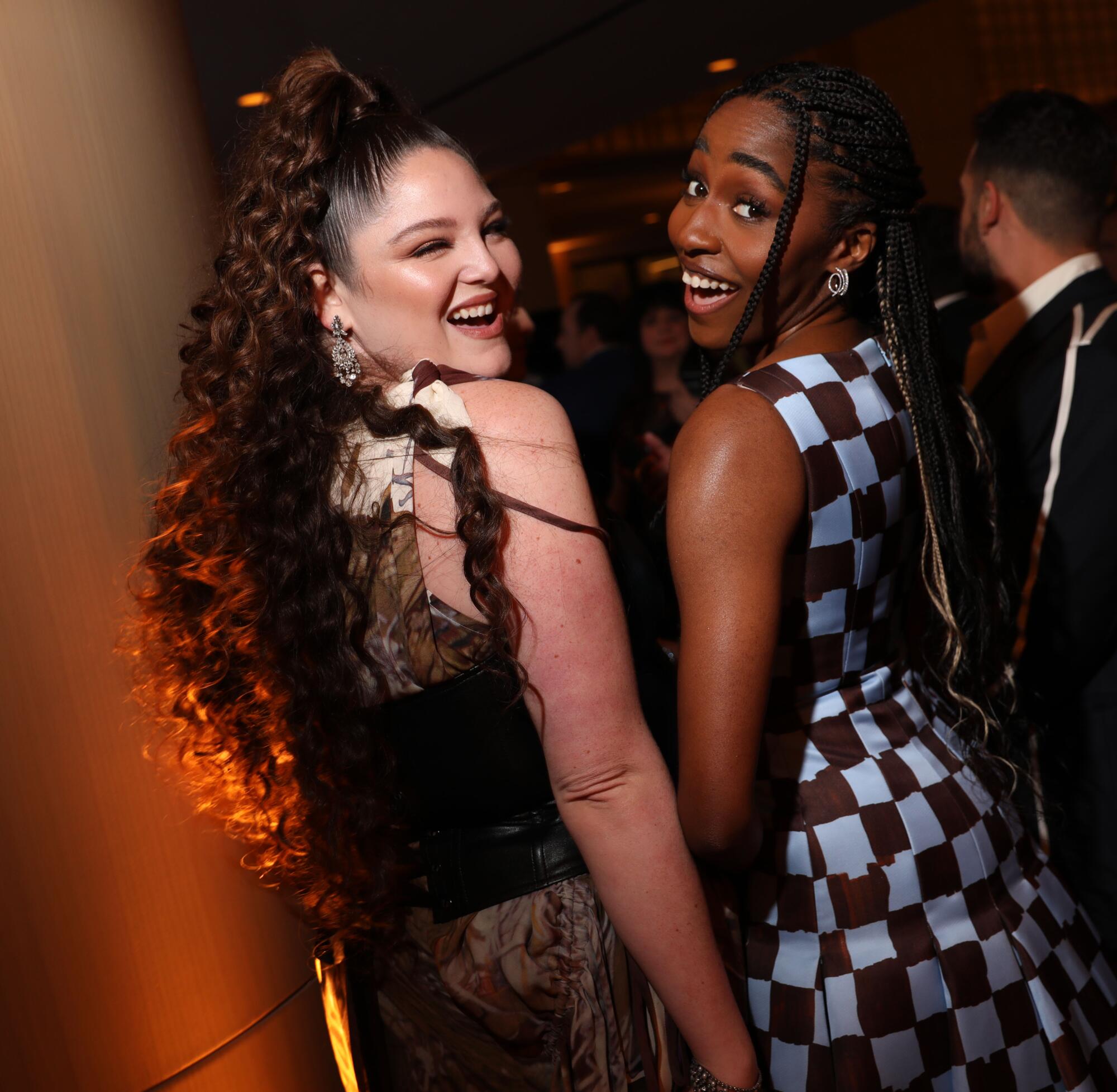 two women in dresses look behind their shoulder and smile 