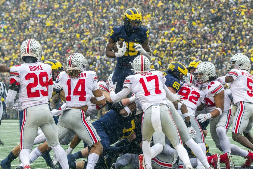 Michigan running back Hassan Haskins (25) leaps over Ohio State defenders for a touchdown in the second quarter of an NCAA college football game in Ann Arbor, Mich., Saturday, Nov. 27, 2021. (AP Photo/Tony Ding)