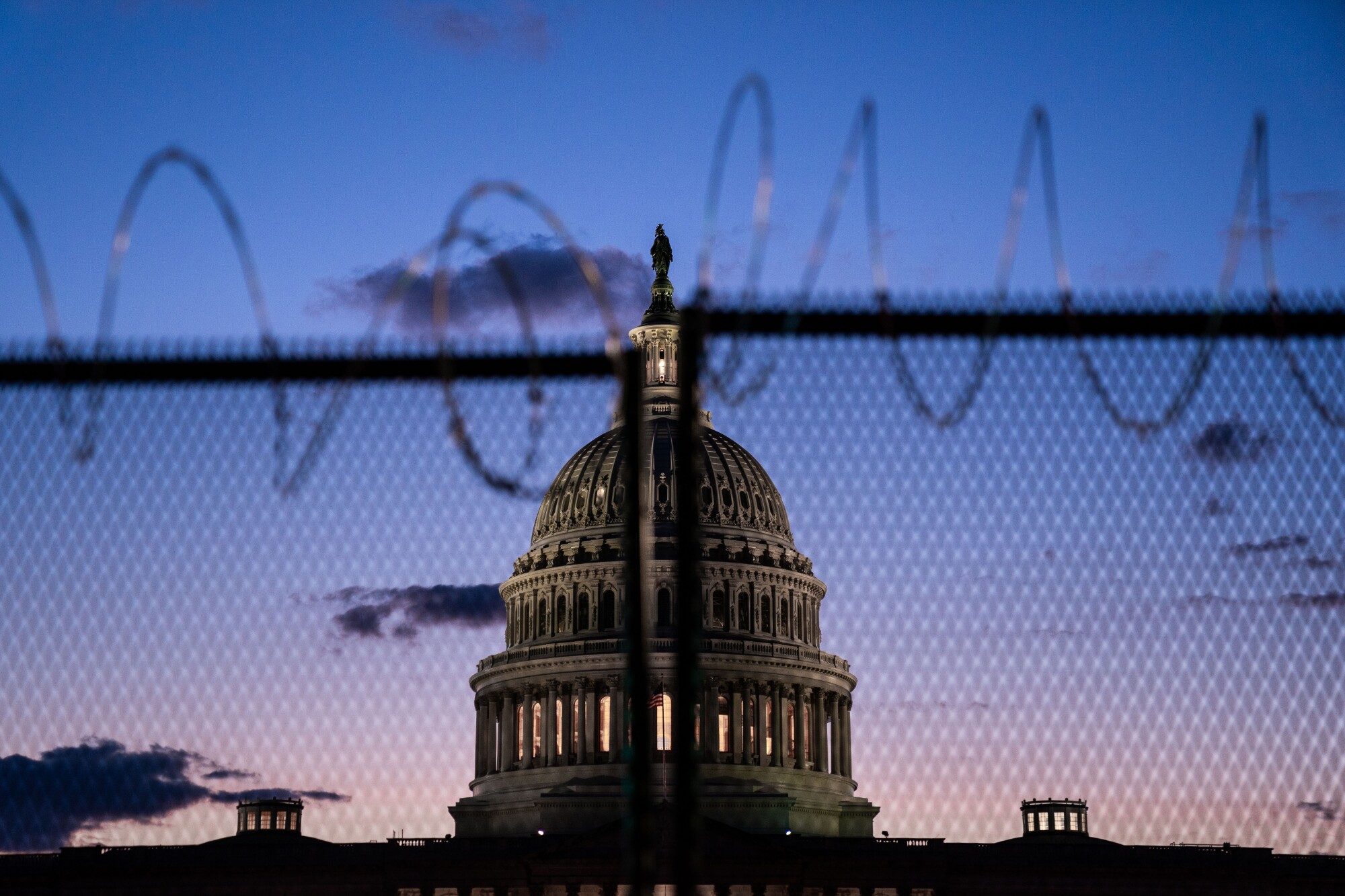 The Capitol dome stands behind a razor wire fence against a purple and pink sunset