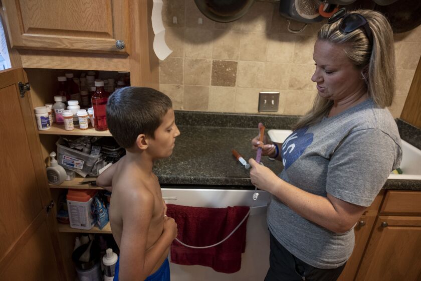 Bo Macan (left) get a dose of Tylenol from his mother Carolyn before heading out to the pool at their home on Thursday, August 1, 2019, in Roeland Park, Kansas. Bo's mother, Carolyn stopped working several years ago to take care of him. She also spends a huge amount of time and energy dealing with medical bills and trying to coordinate fundraisers through GoFundMe to help offset the thousands of dollars of bills the family gets every year because they have high-deductible insurance through Bo's father's work. The Macan’s are a like many Americans who are turning to GoFundMe and other charities and crowd-funding sources, despite having health insurance.