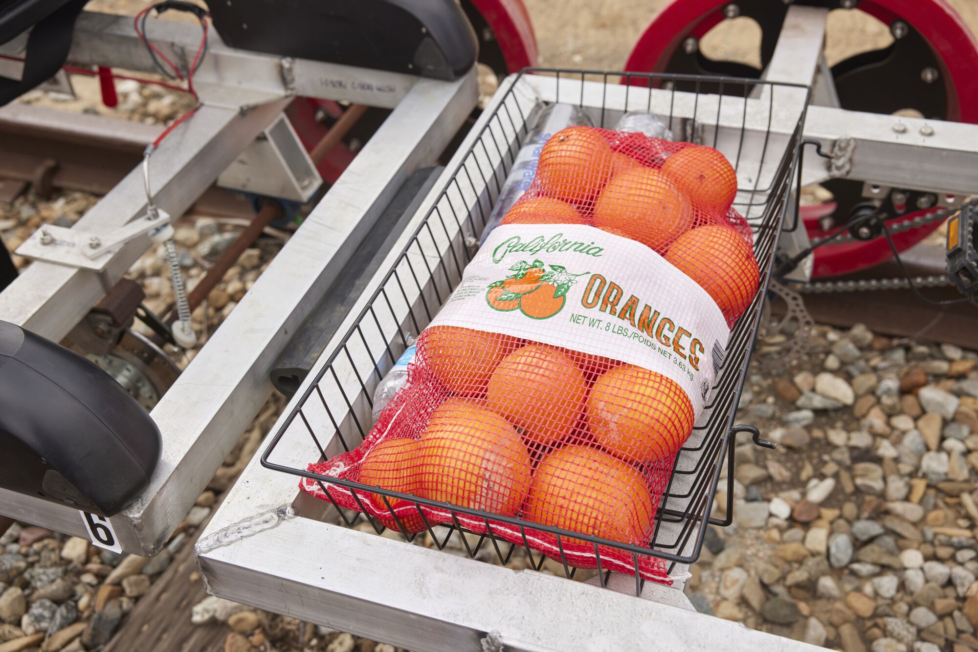 A bag of oranges sitting in a black wire basket on a rail bike.