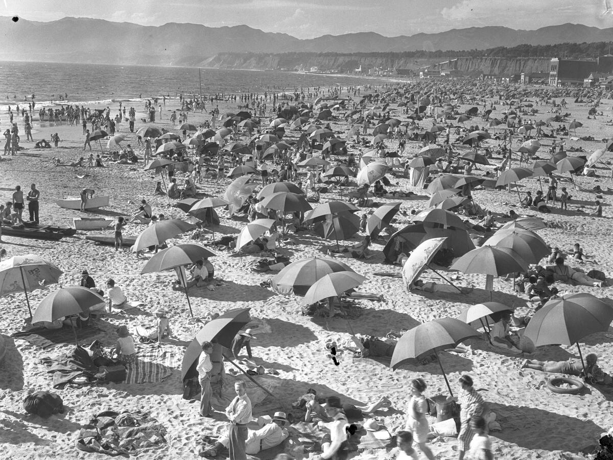 A beach covered with people sitting beneath umbrellas and congregating in the water. 