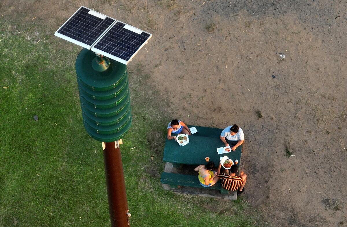 People eat at an outdoor table below a siren tower.