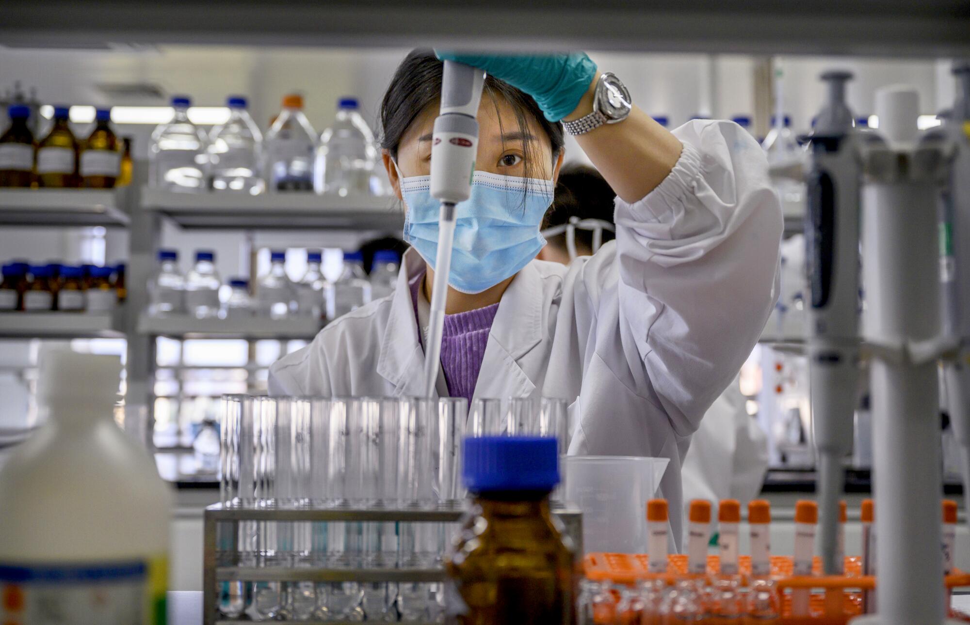 A masked woman works with test tubes in a lab.