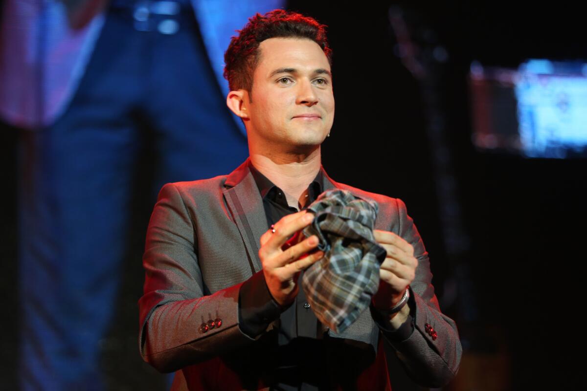 A man in a dark shirt and blazer holds a balled-up piece of fabric in front of him.