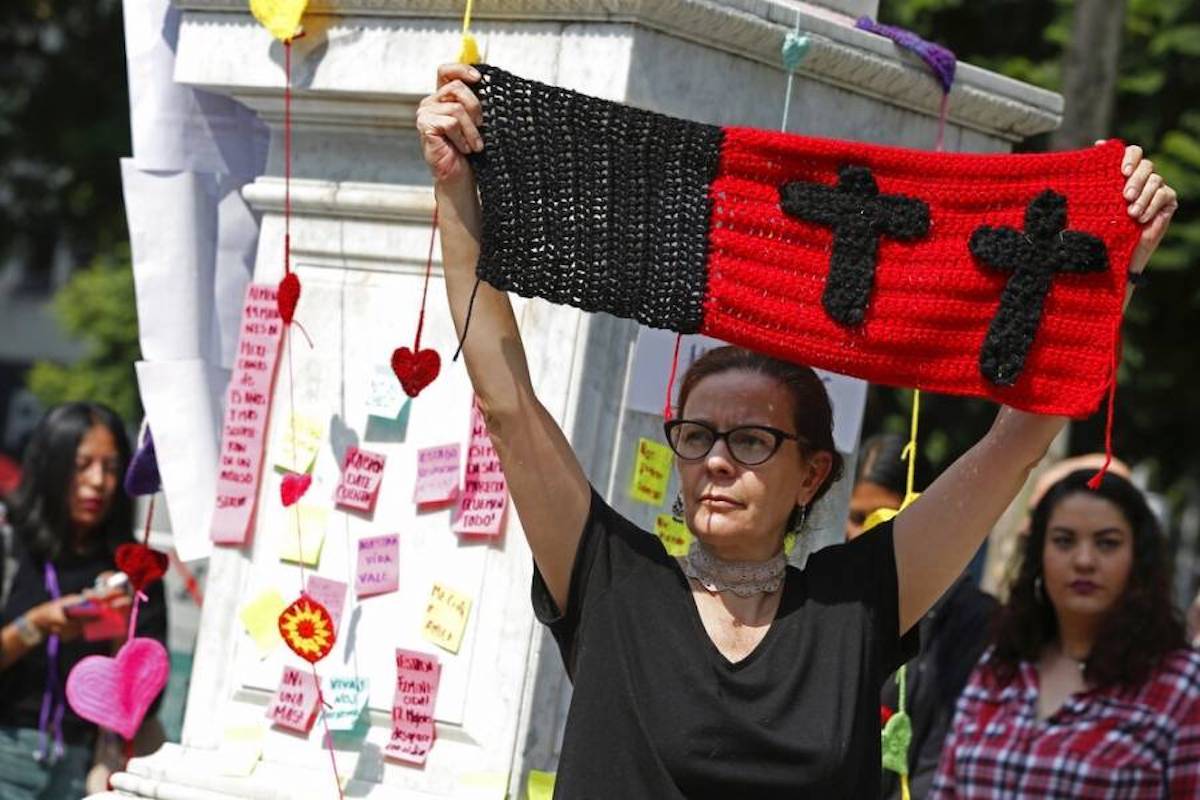 Mónica Ortega levanta un tejido con cruces negras durante un memorial con corazones bordados para las mujeres asesinadas en el parque Alameda en Ciudad de México.
