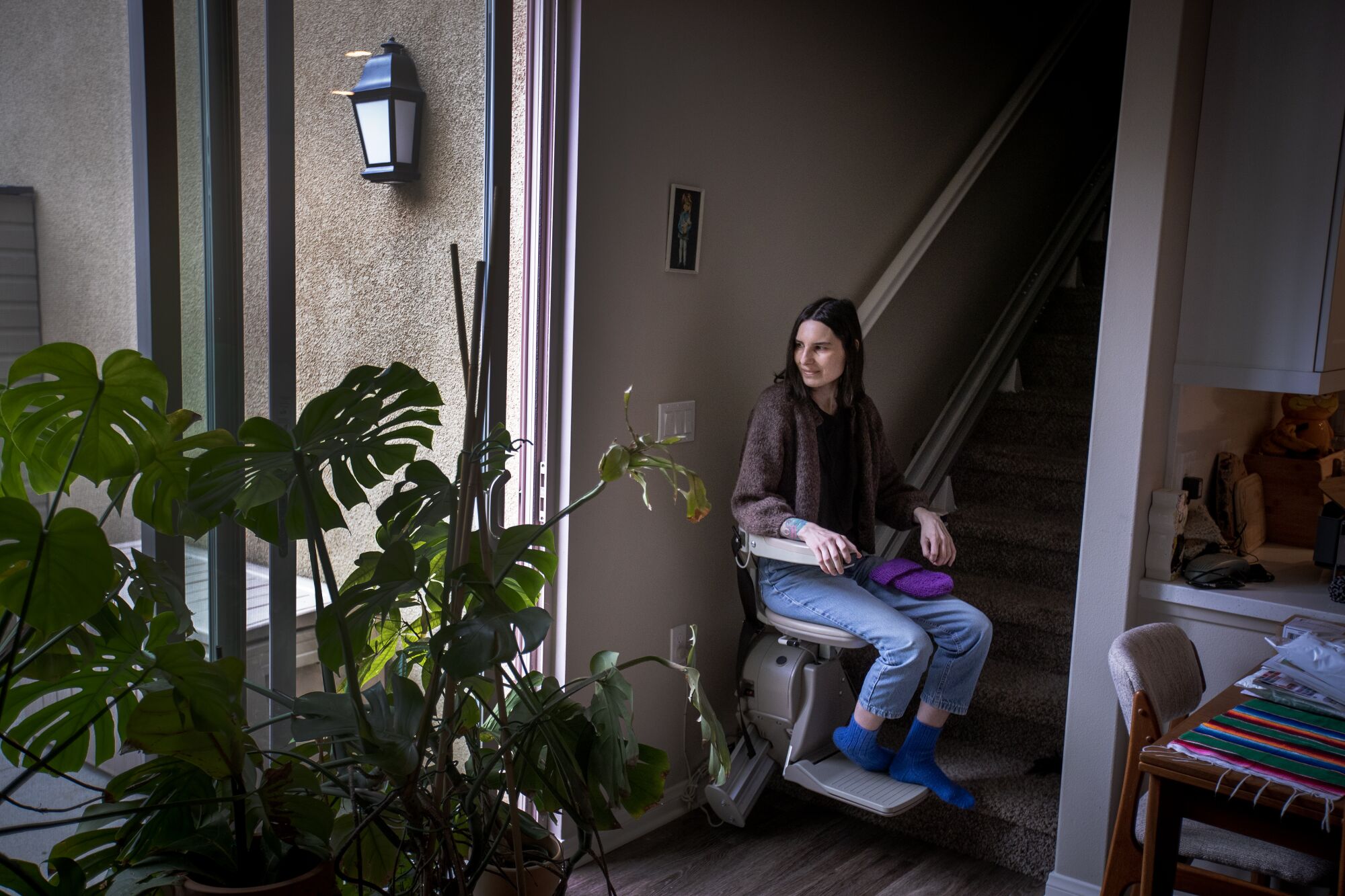 Женщина сидит на кресельном подъемнике у подножия лестницы и смотрит на раздвижные стеклянные двери патио.