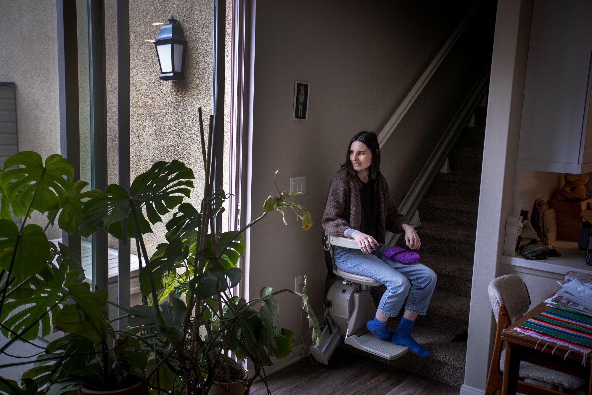 A woman sitting on a chairlift at the bottom of a stairway, looking toward sliding glass patio doors