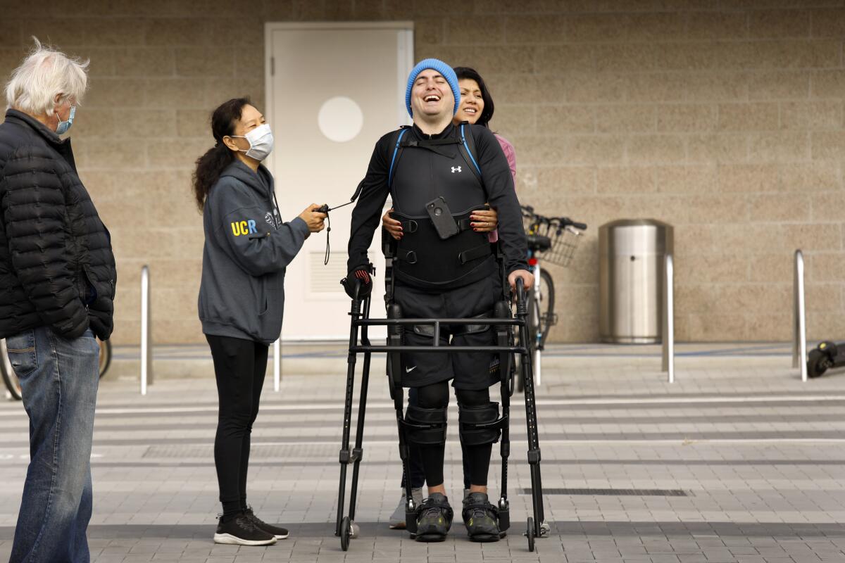 Ignacio Montoya uses a walker, an exoskeleton suit and robotic legs to help him walk along the boardwalk.