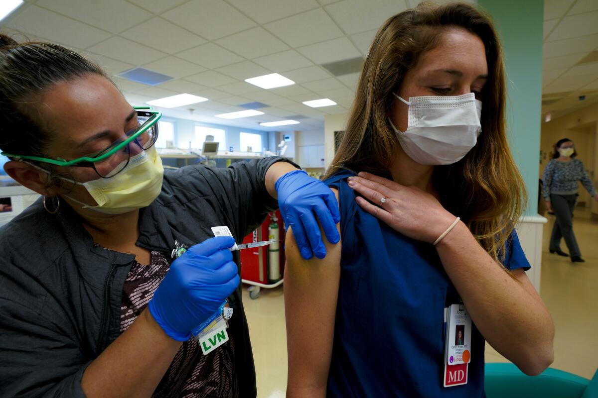 A nurse administers a shot to the upper arm of a doctor.