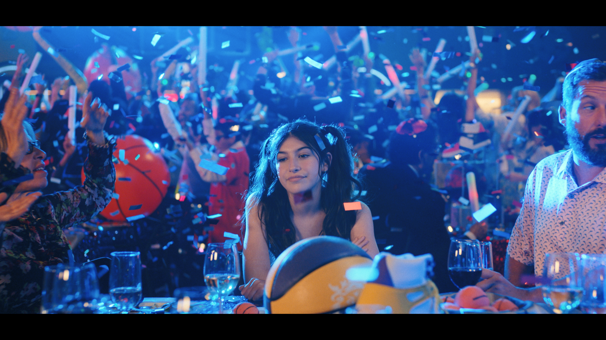 A teenage girl sits alone at a party as confetti falls.