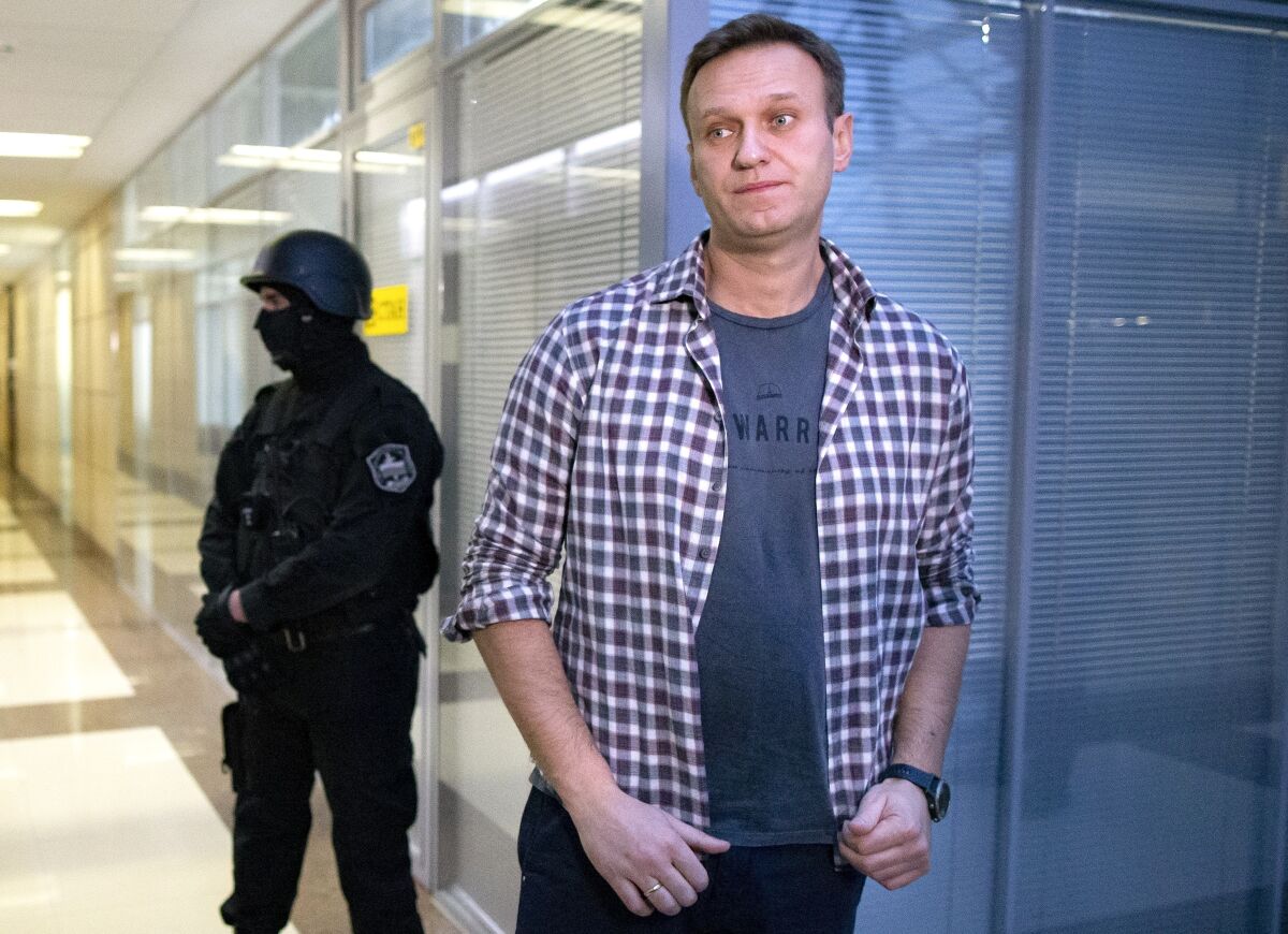 FILE- In this file photo taken on Thursday, Dec. 26, 2019, Russian opposition leader Alexei Navalny speaks to the media in front of security officers standing guard at the Foundation for Fighting Corruption office in Moscow, Russia. Police raids the offices of Alexei Navalny's Foundation for Fighting Corruption in Moscow, Russia, Friday, July 17, 2020. Opposition leader Navalny sees the move as politically motivated.(AP Photo/Alexander Zemlianichenko, File)