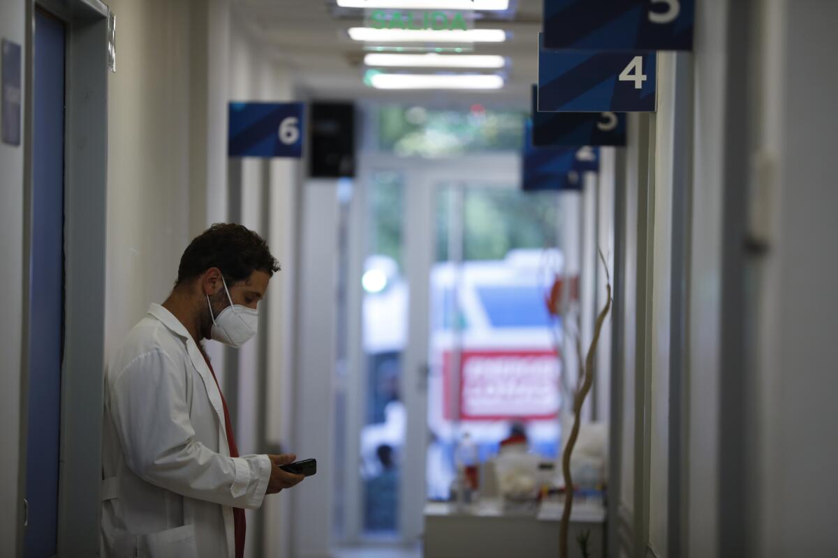 A doctor looks at his smartphone while standing in a hospital corridor 