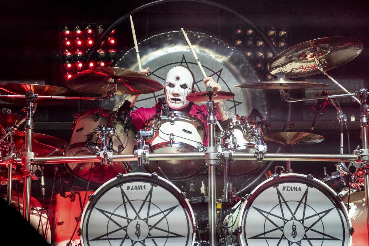 A person in white face makeup sits behind a drumkit onstage