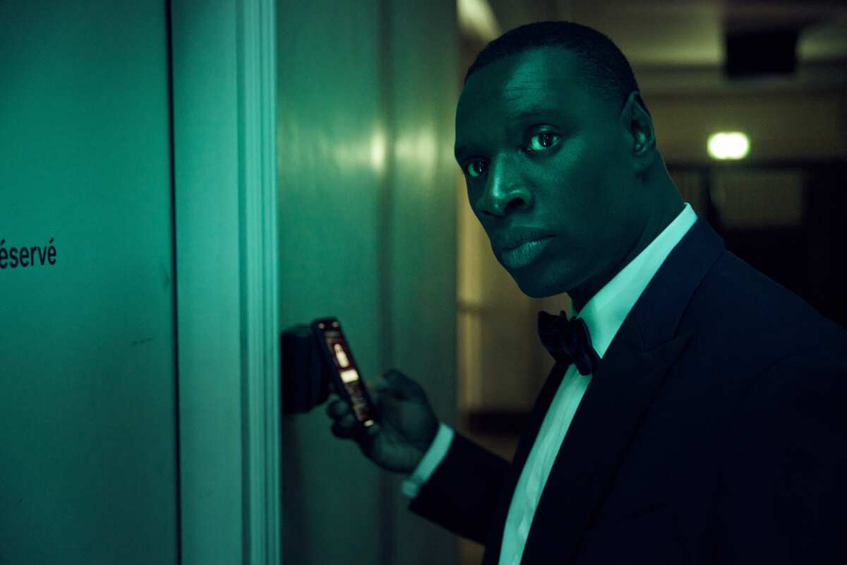 A man in a tuxedo looks down a corridor while holding a cellphone