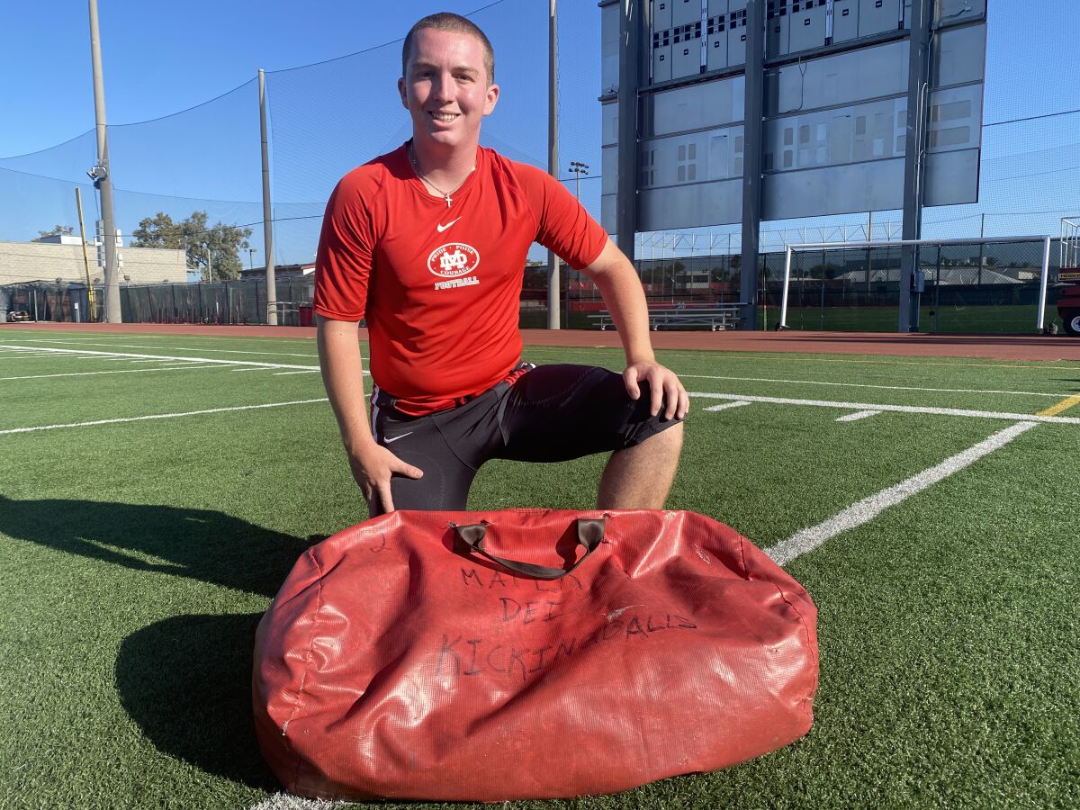 Kicker Chase Meyer kneels on a football field with a red duffle bag at his feet.