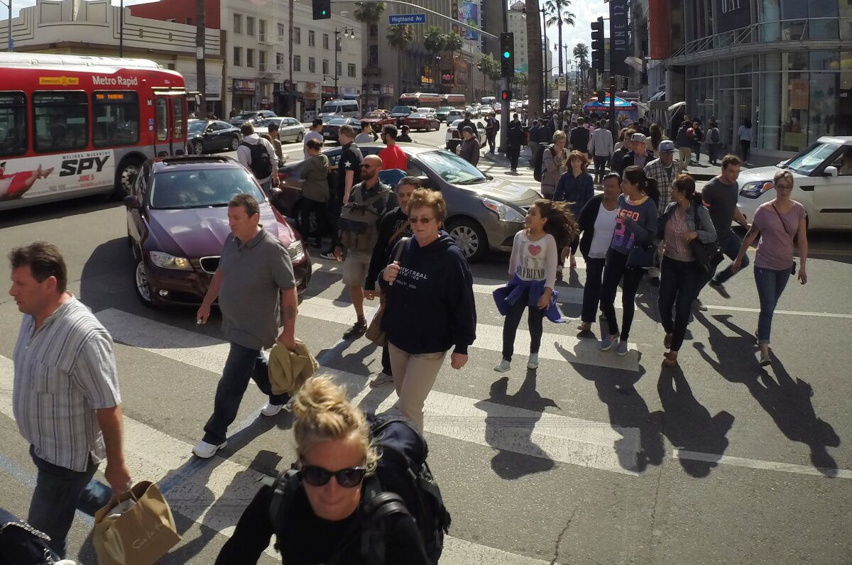 Pedestrians make their way around cars in the crosswalk at the intersection of Hollywood Boulevard and Highland Avenue in Hollywood.