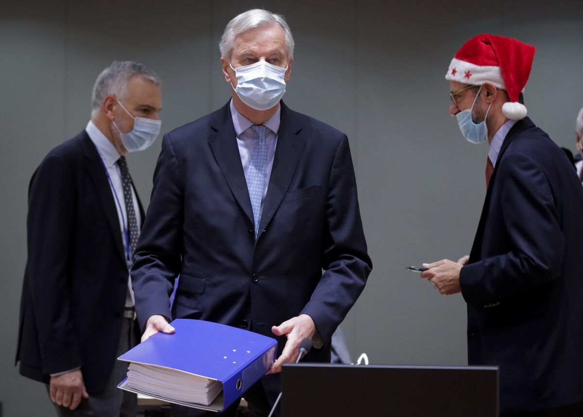 Michel Barnier holds a copy of the post-Brexit trade deal with the U.K. while two men stand behind him.