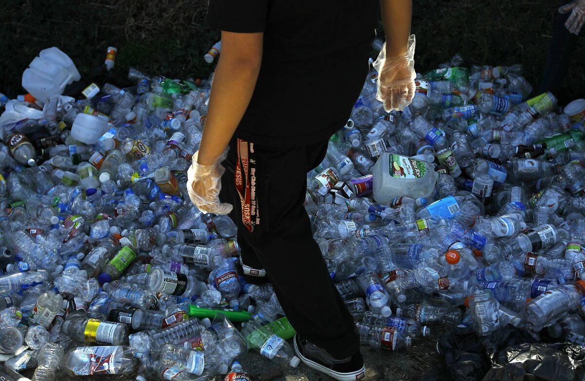 A man walks over a pile of plastic bottles that can no longer be easily recycled. 