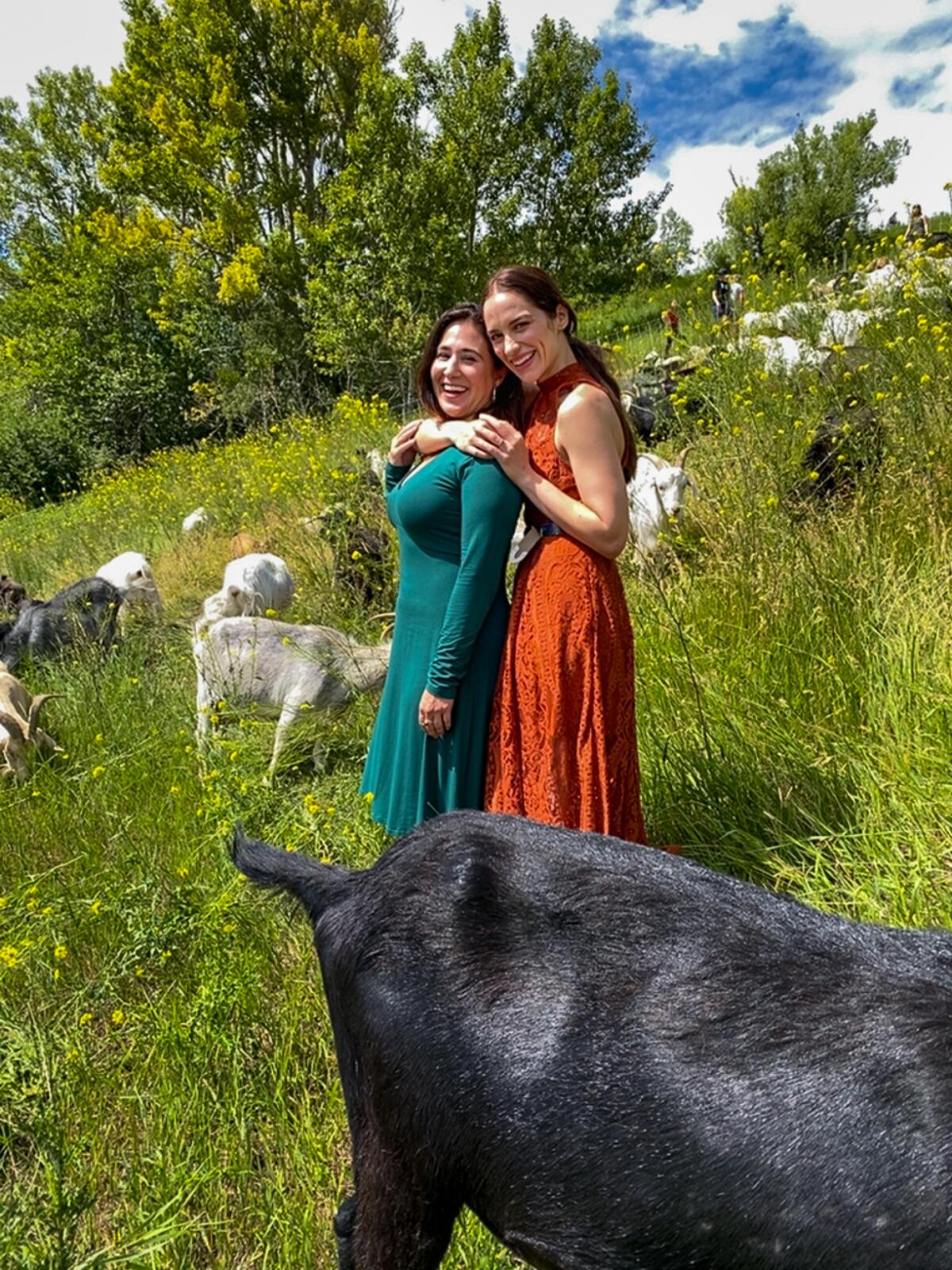 "Wynonna Earp" creator Emily Andras and actress Melanie Scrofano pose on a hillside among goats. 