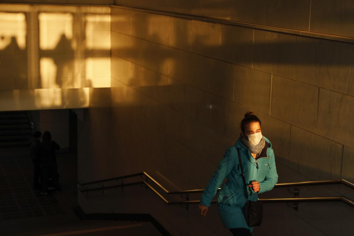 Una mujer con cubrebocas sale de un paso peatonal hacia la calle mientras el sol se pone en Moscú.